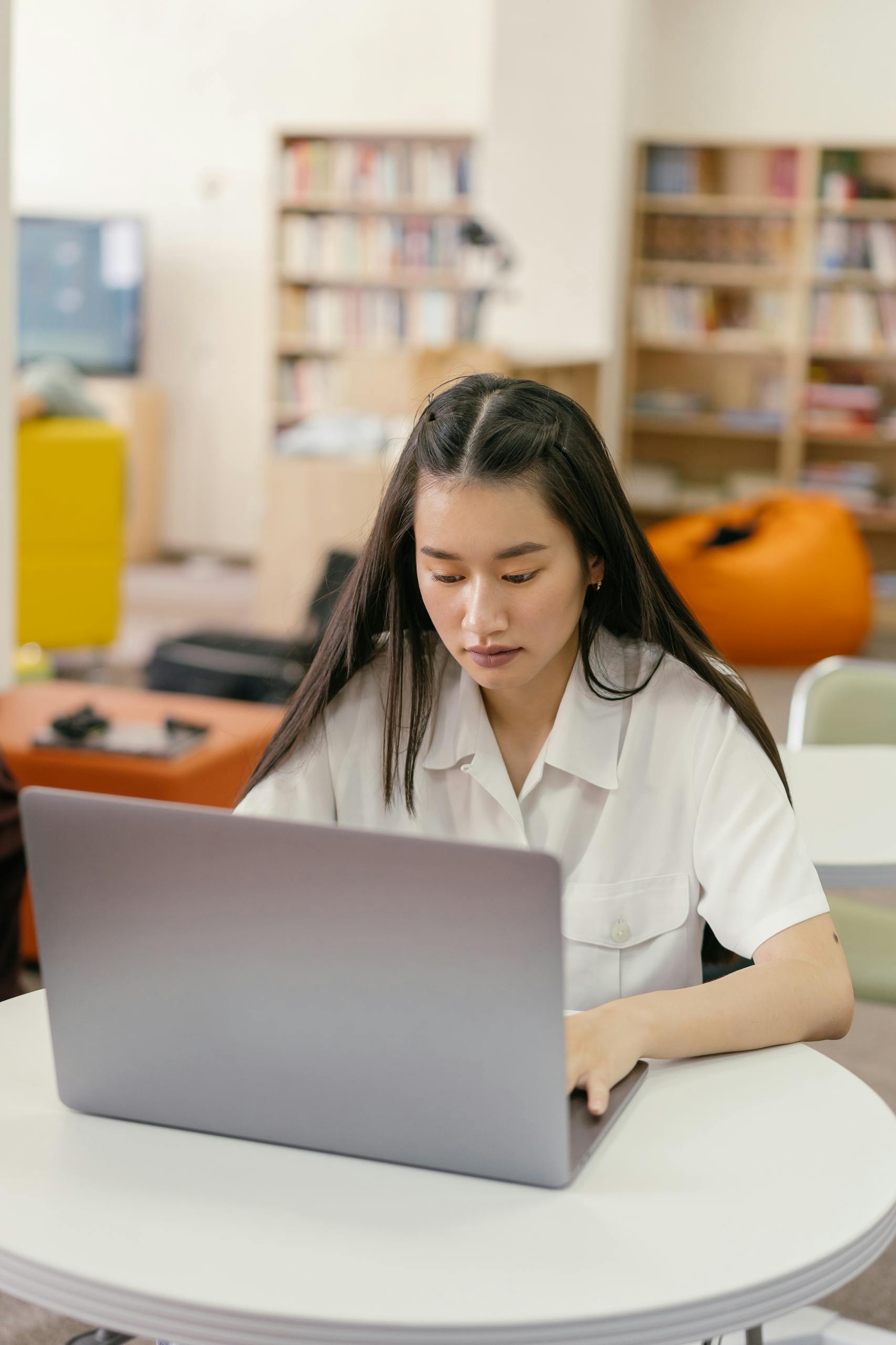 A young woman uses a laptop in a cozy library setting, emphasizing education and technology.